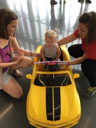Meaghan kneels down to help make adjustments to a child's yellow modified car.